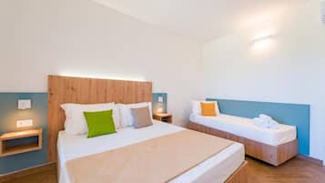 A hotel room with a large bed, a smaller bed, wooden headboards, bedside tables, and a wall-mounted light fixture.