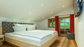 Une chambre à coucher avec un lit en bois, une table de chevet, une fenêtre avec des rideaux et un téléviseur fixé au mur.
