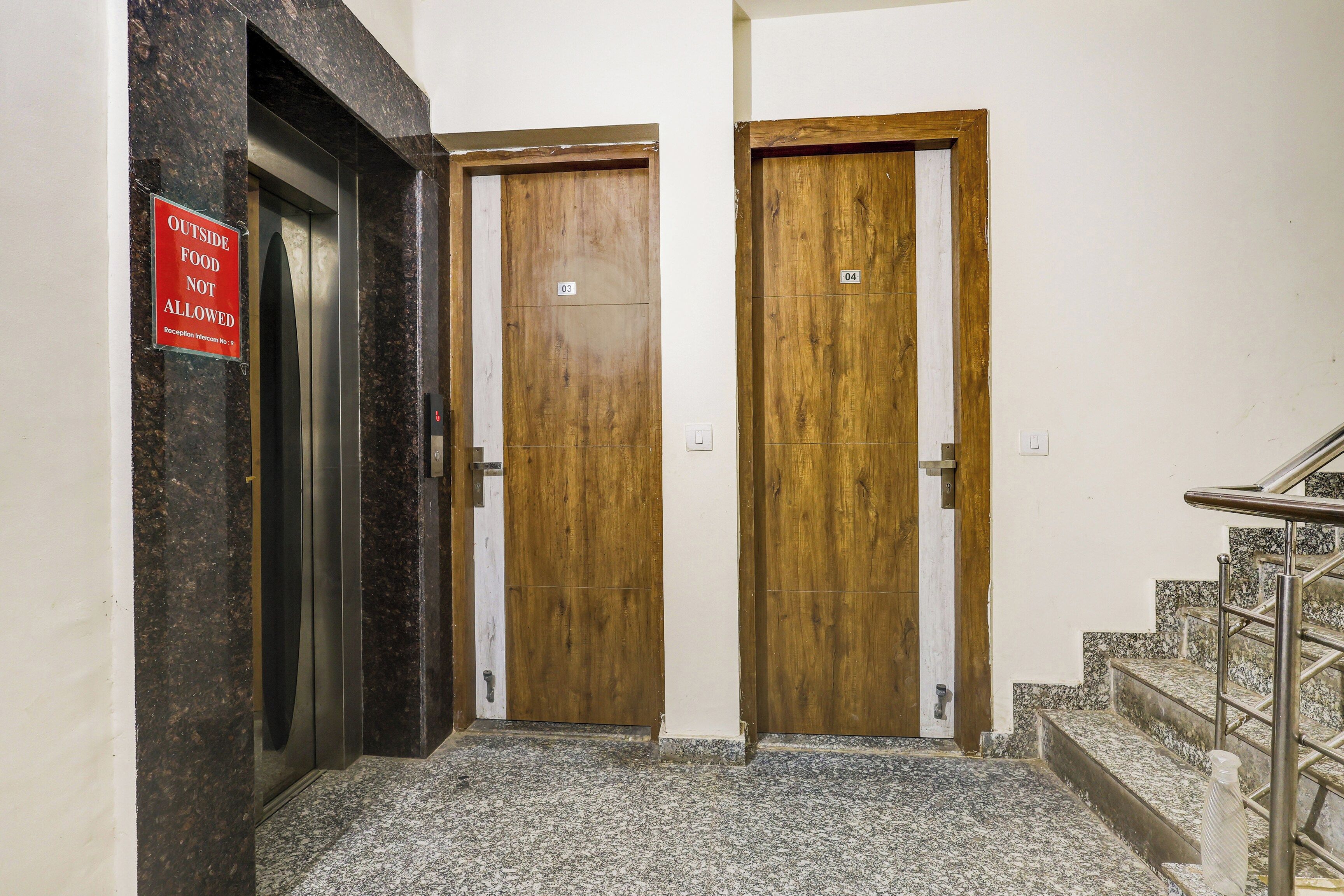 Ein Flur mit zwei Holztüren, eine davon mit einem Schild, das anzeigt, dass fremde Speisen nicht erlaubt sind, und einer Treppe mit Metallgeländern.