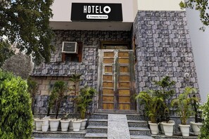 Entrada d'un hotel amb façana de pedra, una porta de fusta i plantes en testos.