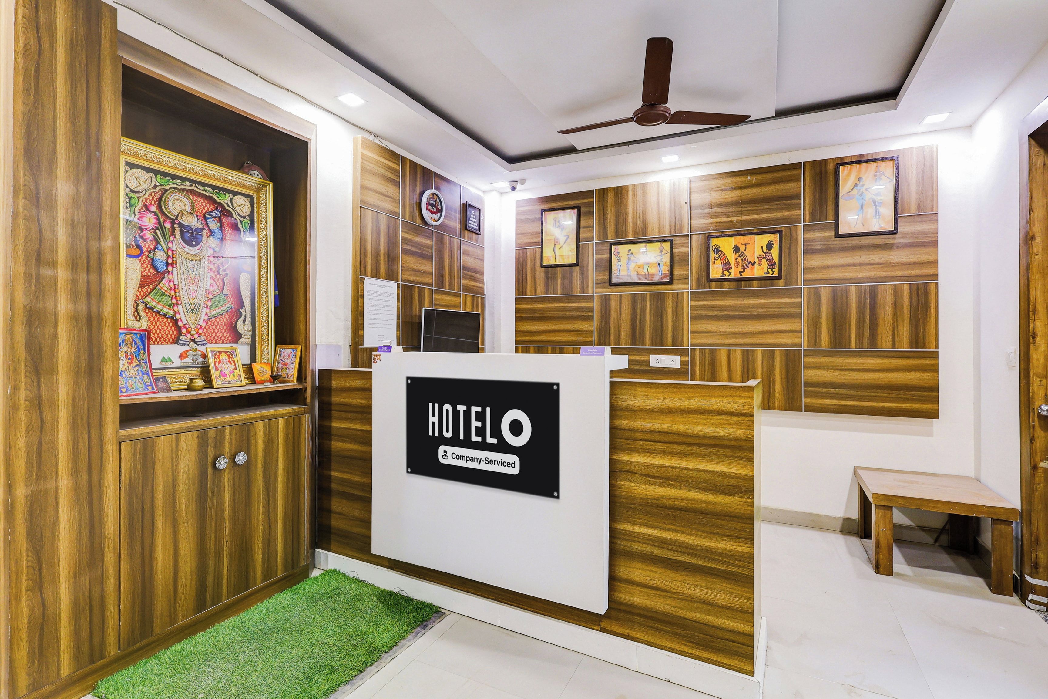 A hotel reception area with a wooden reception desk, a ceiling fan, and framed artwork on the walls.