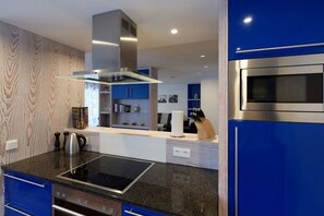 A modern kitchen with a built-in stove, a stainless steel range hood, and blue cabinetry. - Aquamarine Suite KURFÜRST KARL THEODOR (Oberstdorf)