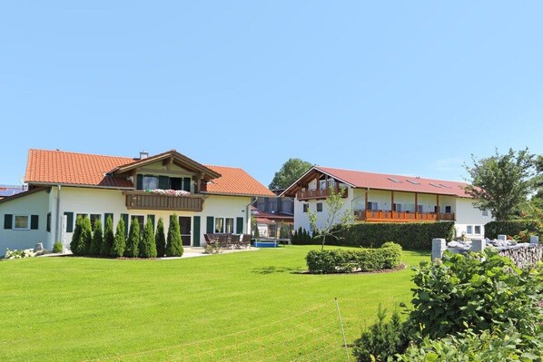 Uma casa de dois andares com telhado de telhas vermelhas, varanda e um gramado bem cuidado.