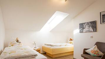 Ein Schlafzimmer mit schräg steilender Decke, einem Bett mit Blumenmuster-Bettwäsche, einem Nachttisch, einem Sessel und einem gerahmten Bild an der Wand.