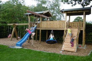 A wooden play structure with a slide, climbing net, and swing.