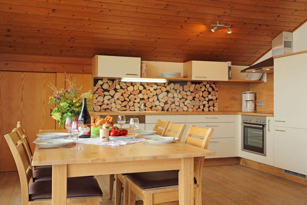Ein Holztisch ist gedeckt mit Tellern, Gläsern und einer Flasche, umgeben von Stühlen.