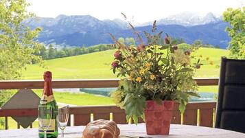 Ein Tisch mit Champagnerflasche, einem Glas und einem Brot auf einer Terrasse mit Blick auf die Berge.