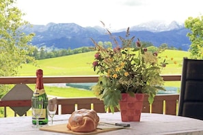 A table with a bottle of champagne, a glass, and a loaf of bread on a terrace with a mountain view.