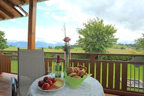 Mesa posta com comida e bebidas numa varanda com vista para uma paisagem deslumbrante.