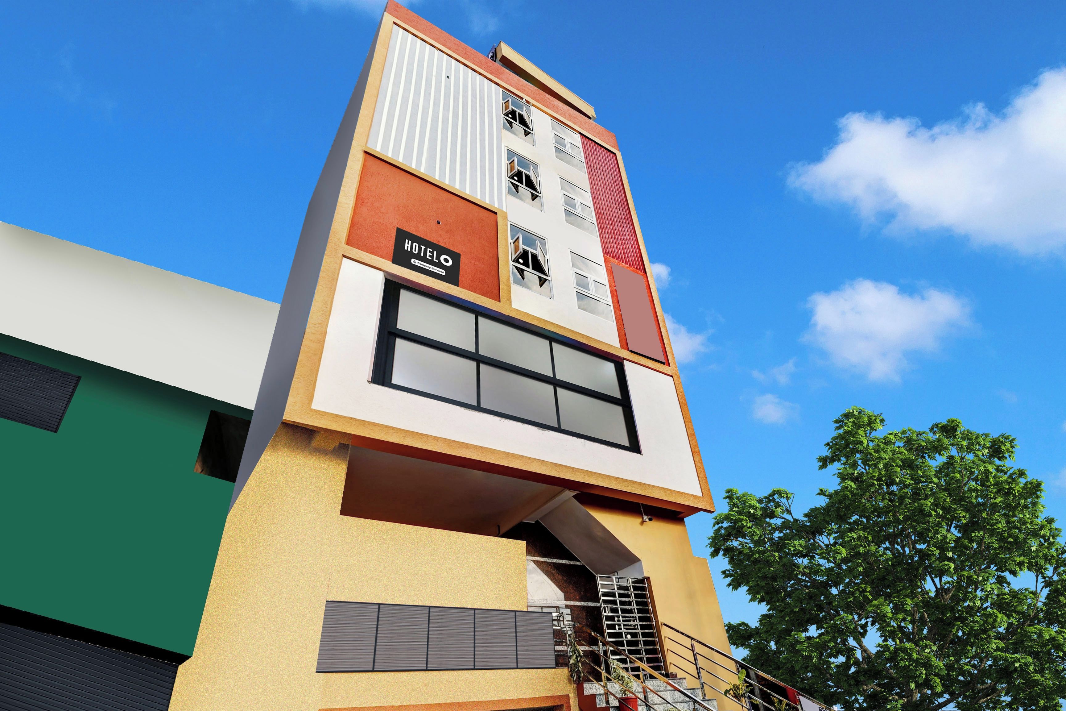 A multi-story hotel with a prominent 'HOTEL' sign on the facade, a staircase leading to the entrance, and a clear blue sky in the background.