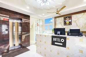 A hotel reception area with a marble counter, a reception desk, a ceiling fan, and a sign indicating the hotel name. - Super Hotel O Vizianagaram (Vizianagaram)