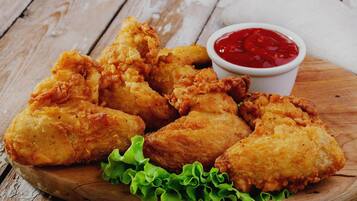Fried chicken pieces on a wooden board with lettuce and a small bowl of ketchup.