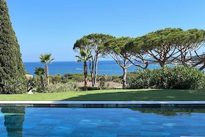 Una piscina con vistas despejadas al mar, rodeada de vegetación y árboles bien cuidados.