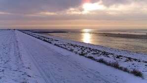 A snow-covered beach with a clear sky and the sun setting or rising over the water. - Holiday apartment with 1 bedroom (Wurster Nordseeküste)