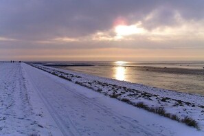 A snow-covered beach with a clear sky and the sun setting or rising over the water. - Holiday apartment with 1 bedroom (Wurster Nordseeküste)