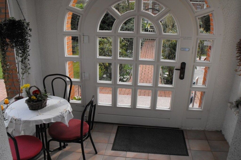 A room with a white door, a small table with a basket of flowers, and red cushioned chairs.