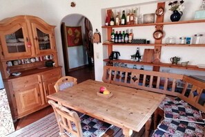 A wooden dining table with chairs, a wooden cabinet with glass doors, and shelves with bottles and glassware. - Lake Constance mountain view with winter garden (Oberstaufen)