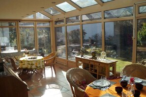Ein Wintergarten mit Essbereich, großen Fenstern und Blick auf den Garten.