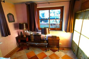 Ein Zimmer mit Fenster, Schreibtisch, Lampe und einem kleinen Schrank.