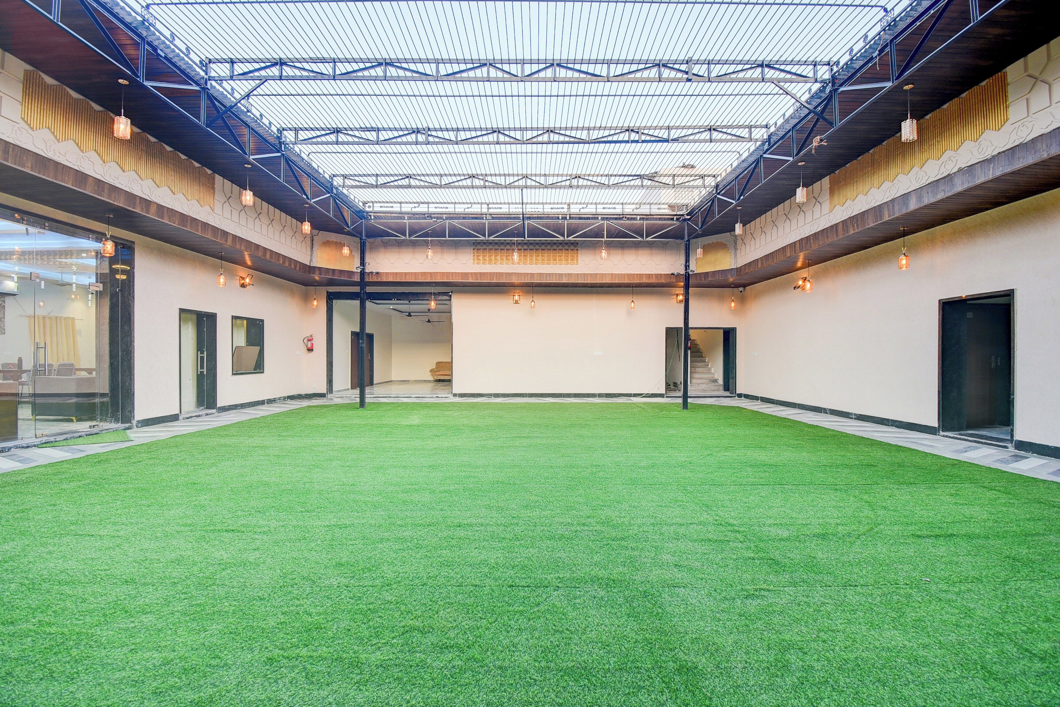 An indoor space with a green artificial turf floor, a high ceiling with a metal framework, and hanging pendant lights.