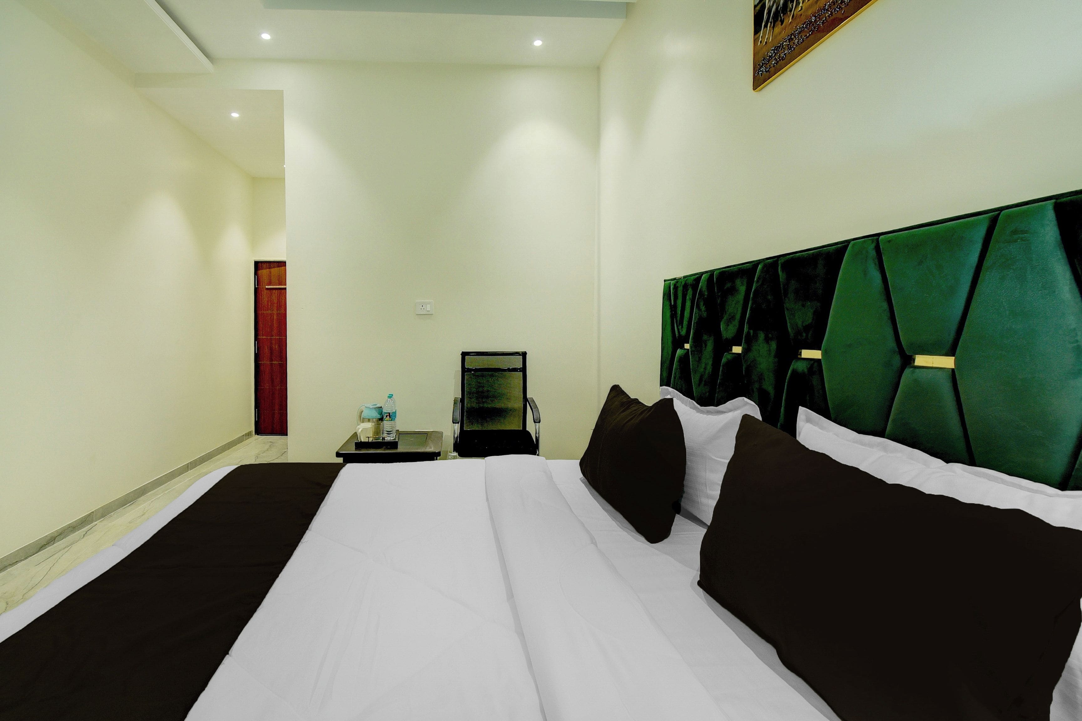 A hotel room with a large bed, a nightstand, a chair, and a painting on the wall.
