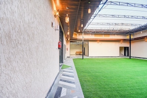 A building with a covered outdoor area featuring artificial grass, a fire extinguisher, and a ceiling with hanging lights. - Collection O Amer Jaipur (Jaipur)