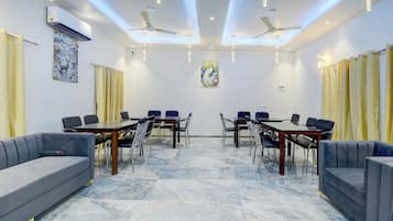 Uma sala de conferências com piso de mármore, dois sofás, uma mesa com cadeiras, ventiladores de teto e obras de arte decorativas nas paredes.