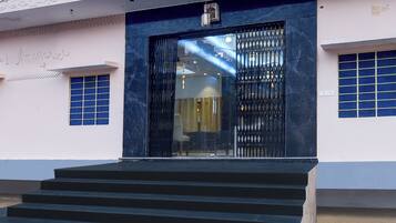 Entrada de un edificio con una reja metálica negra, una escalera que lleva a ella y una ventana con marco azul a la izquierda.