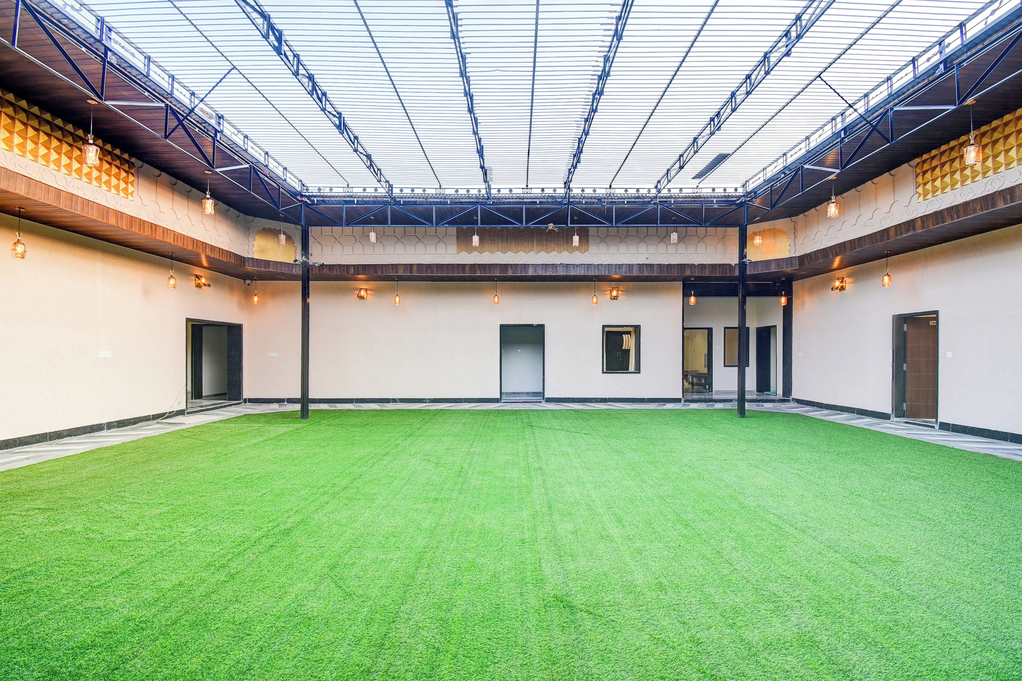 An indoor space with a green artificial turf floor, a high ceiling with a grid-like structure, and multiple doors leading to other areas.