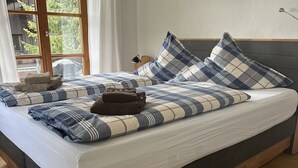 Uma cama com colcha xadrez e travesseiros, cabeceira de madeira e janela com cortinas.
