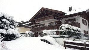 Um edifício com várias andares e varandas, cercado por árvores cobertas de neve e um muro.