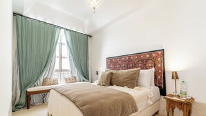 A neatly made bed with a headboard, a bedside table with a lamp, and a window with curtains. - Peaceful 5-Bedroom Riad in the Heart of Marrakech (Marrakesh)
