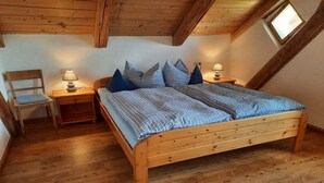 Un dormitorio con una cama de madera, dos mesitas de noche, una silla y un ventanal.