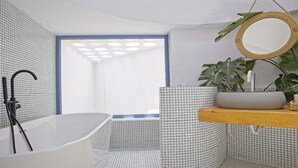 Un bany modern amb una banyera autònoma, un mirall rodó i una planta sobre una prestatgeria de fusta.