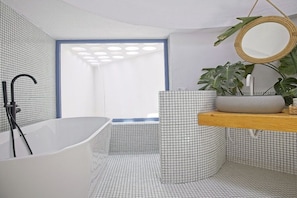 A modern bathroom with a freestanding bathtub, a round mirror, and a plant on a wooden shelf. - Villa in Costa Calma with swimming pool (Costa Calma)