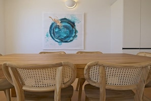 A dining area with a wooden table and woven chairs, a wall-mounted light fixture, and a framed abstract painting. - Villa in Costa Calma with swimming pool (Costa Calma)