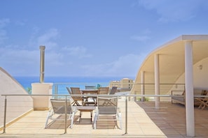 A terrace with outdoor furniture, a clear view of the sea, and a building with a curved roof. - Villa in Costa Calma with swimming pool (Costa Calma)