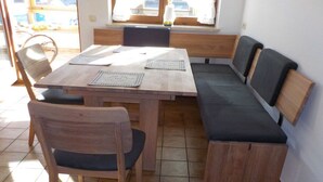 Un coin repas avec une table et des bancs en bois, une fenêtre donnant sur un beau paysage et une bougie sur la table.