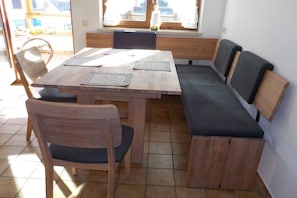 Uma área de refeições com mesa de madeira e bancos, uma janela com vista e uma vela sobre a mesa.