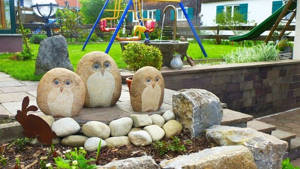 Un jardin agrémenté de statues de hiboux décoratives, une aire de jeux avec des balançoires et des toboggans, et un mur en pierre.