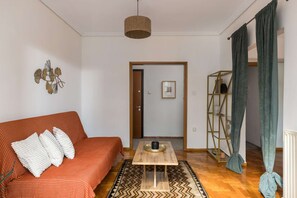 A living room with a sofa, a coffee table, a rug, and a door leading to another room. - Andromeda: Cozy 2BD apartment in the center with spacious balcony (Thessaloniki)