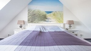 Ein Schlafzimmer mit einem großen Bett, einem Fenster mit Blick auf den Strand und Nachttischen mit Lampen.