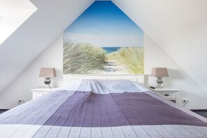 Ein Schlafzimmer mit einem großen Bett, einem Fenster mit Blick auf den Strand und Nachttischen mit Lampen.