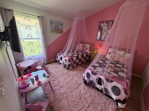 Ein Schlafzimmer mit zwei Betten, einem Schreibtisch und einem Fenster mit Vorhängen.