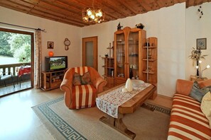 Ein Wohnzimmer mit Fernseher, einer Couch, einem gestreiften Sessel, einem Holzschrank und einem gemusterten Teppich.
