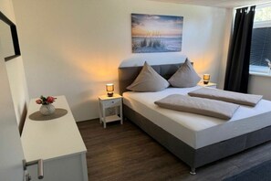 Ein Schlafzimmer mit einem Bett, Nachttischen, einem Wandbild und einem Fenster mit Vorhängen.