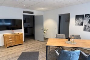 A modern dining area with a wooden table, grey chairs, and a flat-screen TV mounted on the wall. - Holiday apartment with 1 bedroom (Ludwigswinkel)
