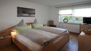 Ein Schlafzimmer mit einem Bett, Nachttischen, einem Fernseher und einem Fenster mit Vorhängen.