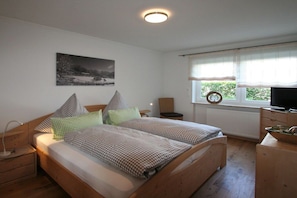 Quarto com cama, mesas de cabeceira, televisão e janela com cortinas.