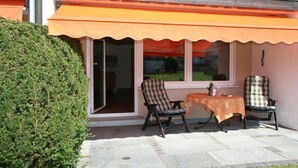 Eine Terrasse im Freien mit zwei Stühlen, einem Tisch, einem Holzzaun und einer Hecke.